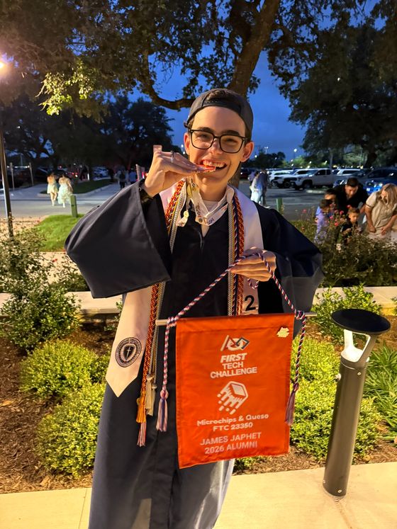 James at graduation holding a FIRST Tech Challenge Microchips and Queso 23350 alumni banner