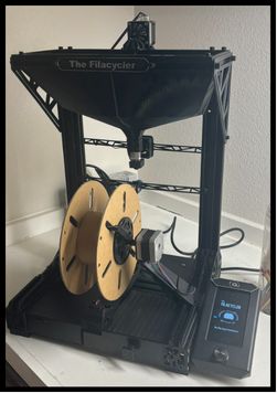 The Filacycler: a black desktop recycler with a funnel on top, a wooden filament spool and a touchscreen