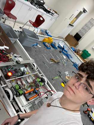 James taking a selfie next to a half-built robot drivetrain with motors and wiring