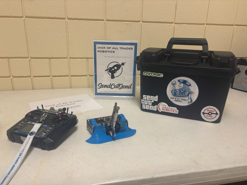 The David Spade antweight, its transmitter and the team pit table with a SendCutSend sponsor sign